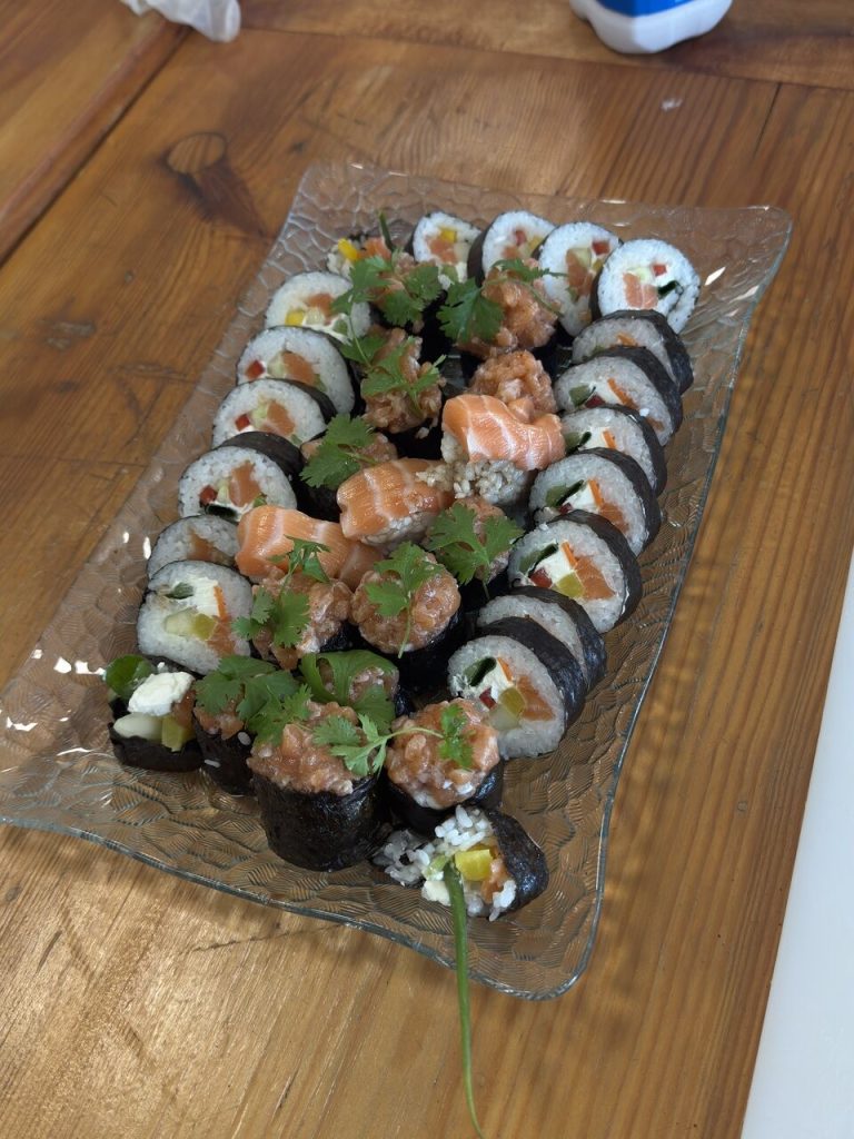 Talerz sushi z różnorodnymi rolkami, w tym z łososiem, warzywami i kolendrą, na drewnianym stole.