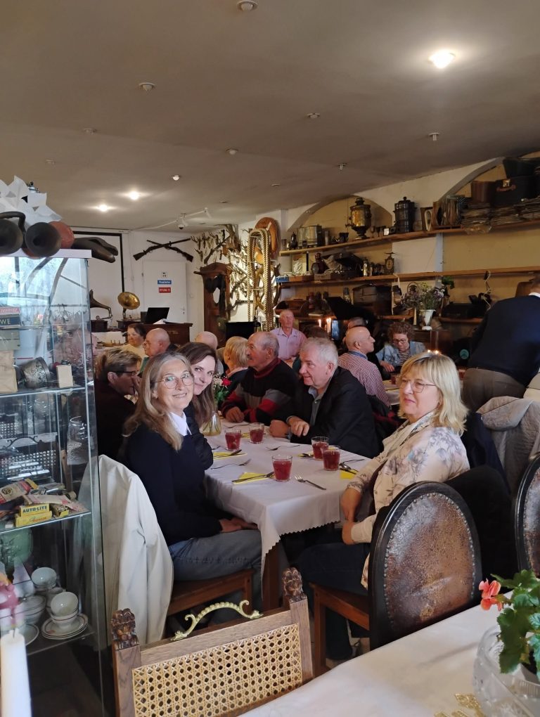 Grupa ludzi siedzących przy stole w restauracji, otoczeni dekoracjami i przedmiotami vintage.