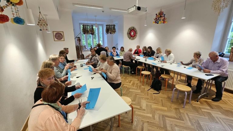 Warsztat rękodzielniczy z uczestnikami pracującymi nad projektami z niebieskiego papieru w jasnym pomieszczeniu.