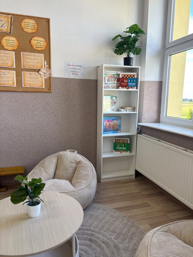 Przytulny kącik z regałem pełnym książek, miękkimi siedziskami i rośliną, idealny do relaksu i czytania.